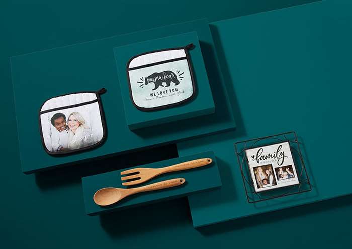 Custom kitchenware products laid out on green background including personalized wooden utensils and custom pot holders