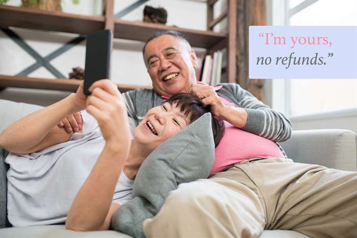 Portrait of a senior couple relaxing on the sofa, the senior woman has her head on her husband's lap whilst the both look at her smartphone together smiling with funny anniversary quote overlay