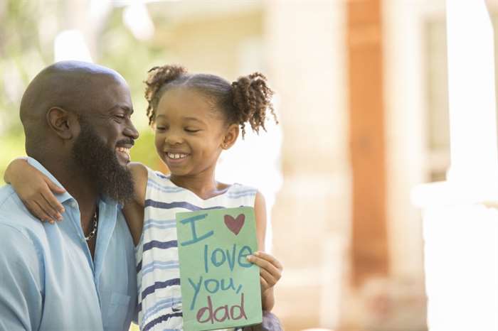 Happy Father's Day. Little girl gives homemade card to her dad in front yard of family home.