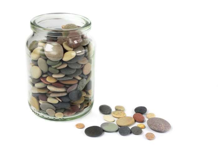 Pebbles or Beach stones in a glass jar on white background.