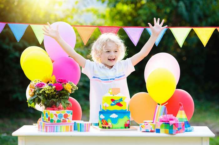 Kids birthday party. Child blowing out candles on colorful cake. 