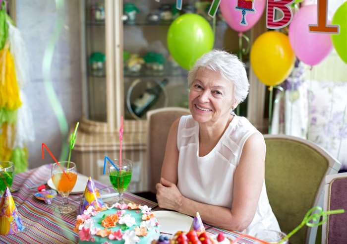 Người phụ nữ lớn tuổi tươi cười trong bữa tiệc sinh nhật lần thứ 80 với đồ trang trí nhiệt đới.