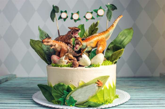 Bánh sinh nhật khủng long dành cho trẻ em được trang trí bằng những bức tượng nhỏ của khủng long trong khu rừng rậm kỷ Jura.