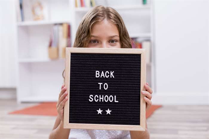 Cute smiling schoolgirl holding and covering with a letter board and smiling. Back to school concept. Family lifestyle indoors