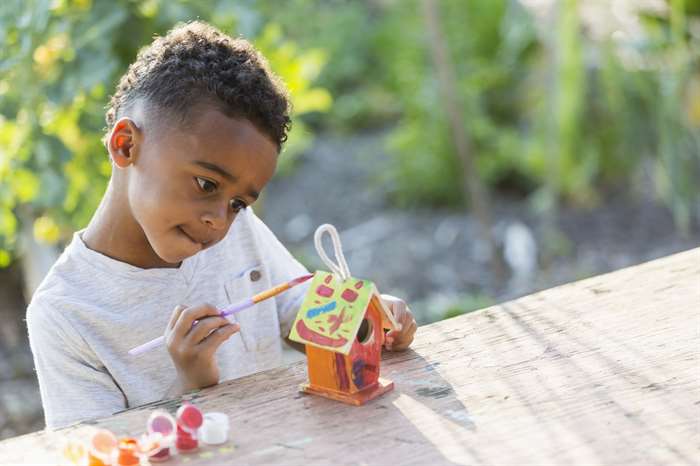 Little boy painting bird house at nature themed summer camp