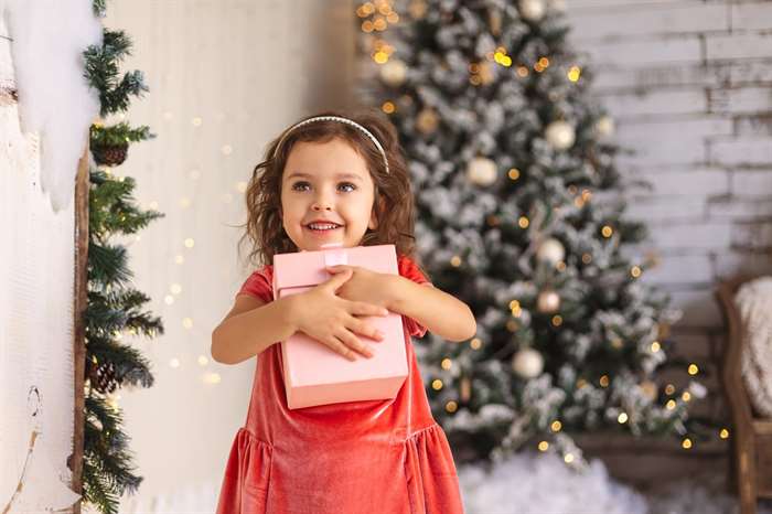 Cô bé vui vẻ đang ôm món quà Giáng sinh trên cây thông Noel và nền đèn.