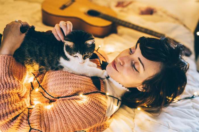 Người phụ nữ nằm trên giường với con mèo và quấn đèn Giáng sinh.