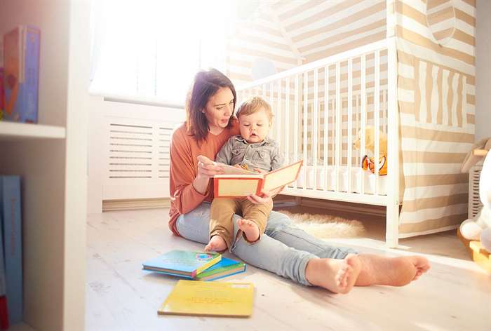 Mom and son sitting on floor by crib reading book.