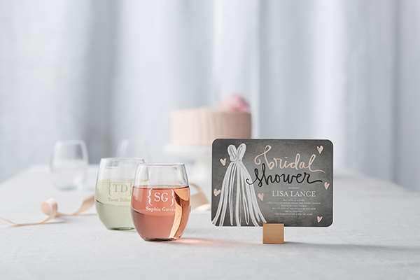 black and pink bridal shower invitation on counter next to wine glasses