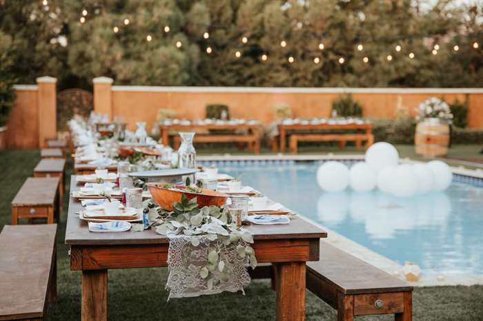 Không gian tổ chức đám cưới theo phong cách tối giản ở sân sau - bàn gỗ với lối trang trí phóng túng xung quanh hồ bơi.