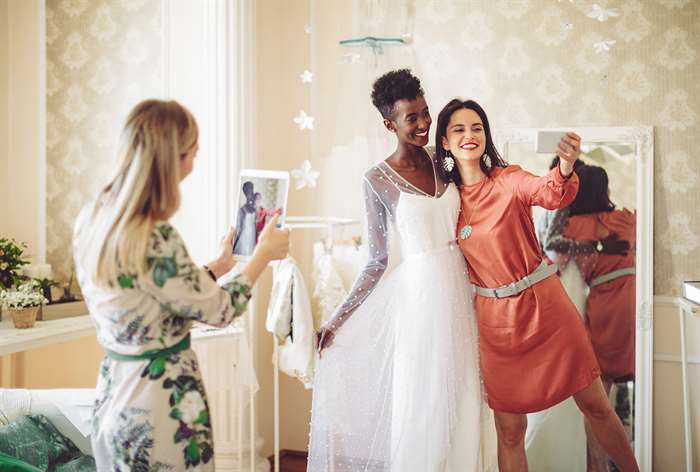 Bride and bridesmaids trying on dresses.