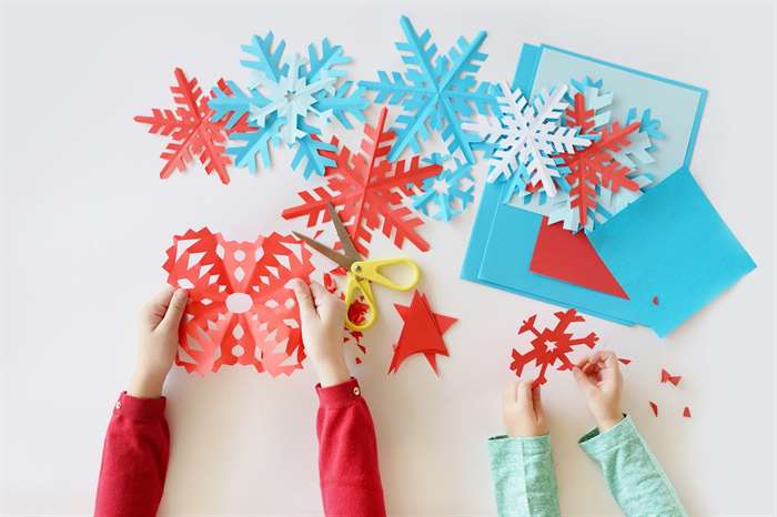 Children's hands cut out on a white background blue and red snowflakes from paper.