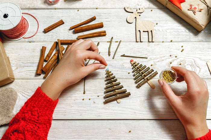 Girl in a cozy knit sweater creates a Christmas tree made of wooden shelves on a white wooden desk.