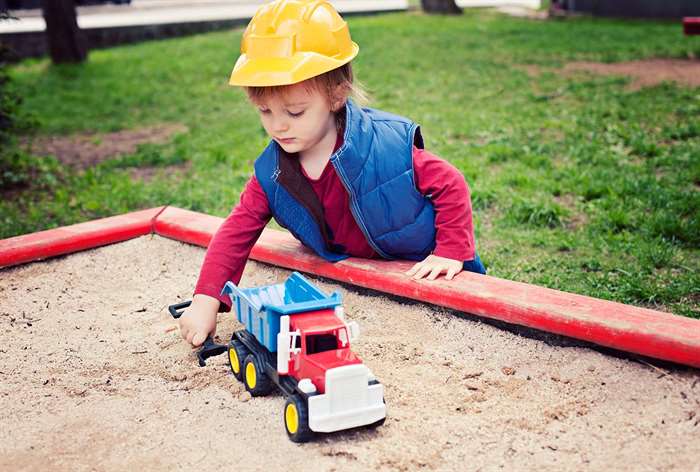 Toddler playing with dump truck in sandbox.