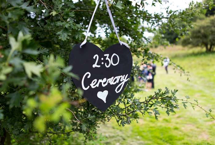 Heart-shaped chalkboard sign hanging from tree.