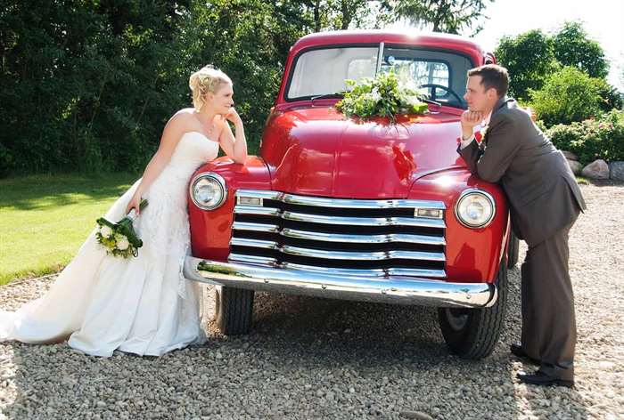 Married couple standing next to red vintage truck.