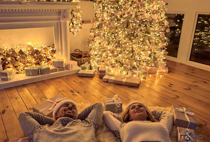 Couple laying on floor next to brightly lit Christmas tree.