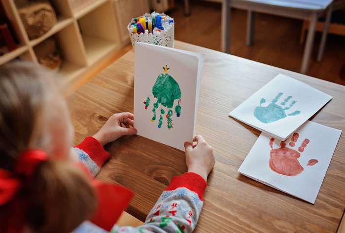 Child holding piece of paper with green painted handprint.