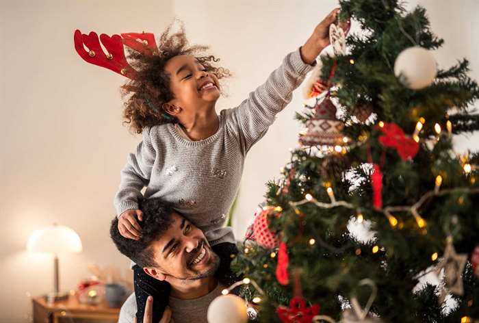 Father and daughter hanging ornaments on tree.