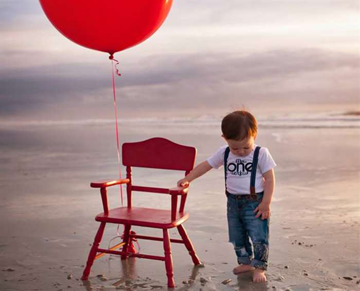 em bé trên bãi biển với quả bóng bay màu đỏ