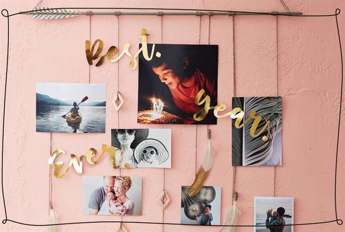 Photos hang from an arrow on strings against a pink background