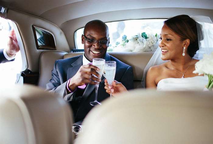 Cặp vợ chồng mới cưới ngồi ghế sau xe nâng ly chúc mừng 