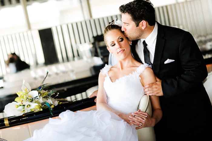 bride sitting while groom kisses her forehead