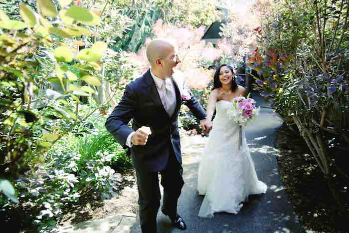 groom leading smiling bride down a garden path