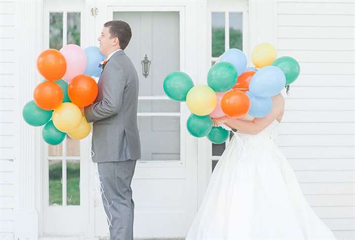 Bride and groom holding balloons in front of faces 