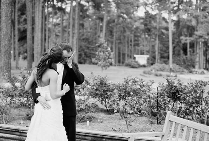 Groom wiping away tears as he holds bride in a garden