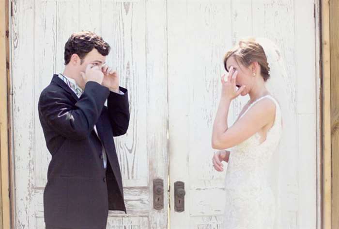 Bride and groom both wiping away tears in front of rustic doors