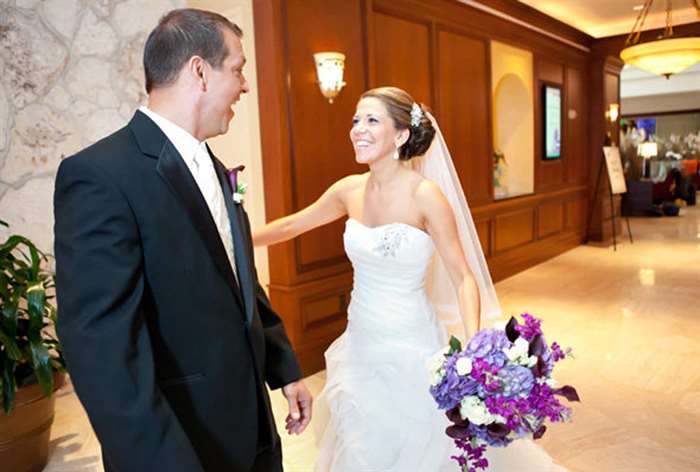 Bride holding purple bouquet looking at groom