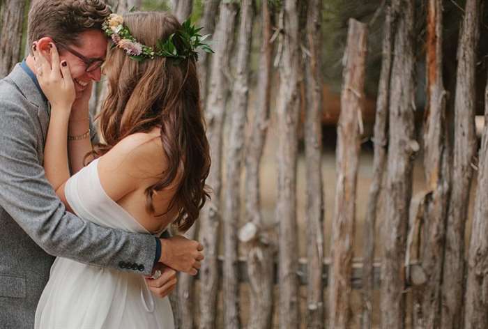 Bohemian bride and groom hugging in front of fence