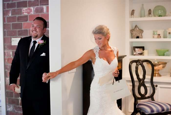 Bride holding groom's hand around the corner of a white wall