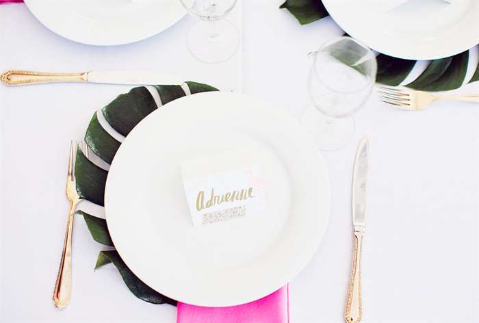 White plates on palm leaves with pink napkins and gold flatware 