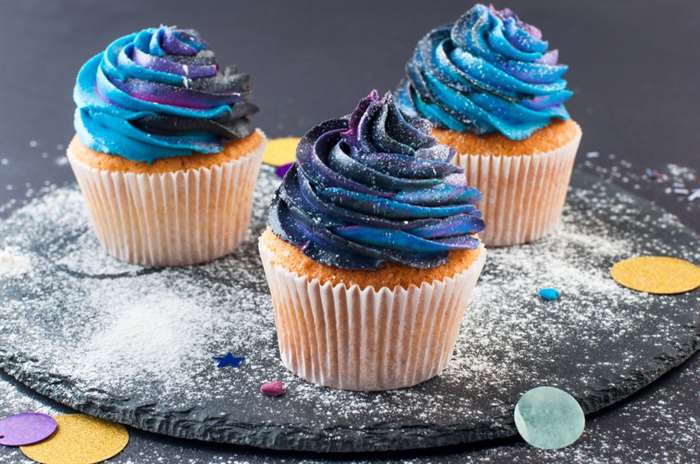 Bánh cupcake vani với kem đánh kem đậm màu thiên hà trên nền tiệc đen.