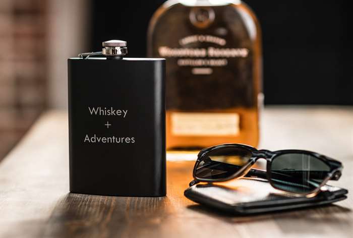 matte black flask that says whiskey and adventures