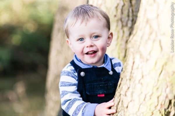 Cậu bé đáng yêu mắt xanh đang ôm một thân cây lớn trong Công viên Bushy TW12 phía tây nam London