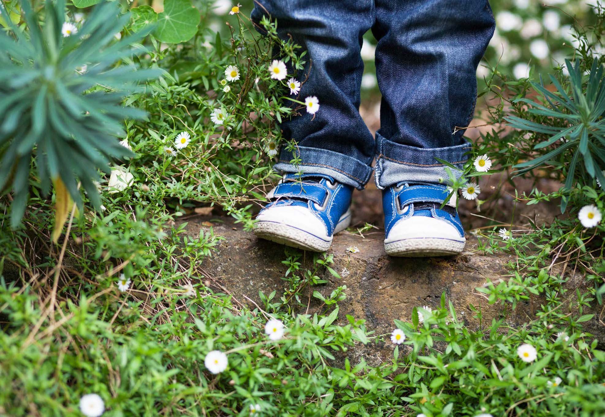 ảnh chụp cận cảnh bàn chân của cậu bé trên mặt đất với hoa trắng và cỏ xung quanh