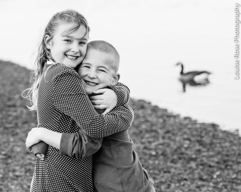 em gái và em trai của cô ấy ôm nhau nhìn vào máy ảnh bên hồ nước ngoài trời