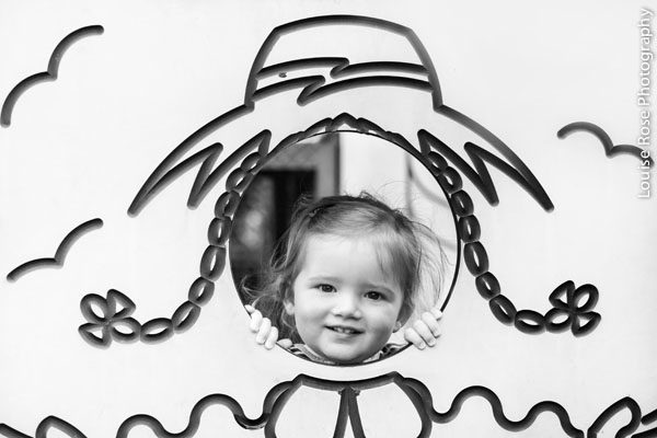 Cô gái nhỏ vui vẻ với khuôn mặt trong tấm ván lỗ trong bức ảnh đen trắng.